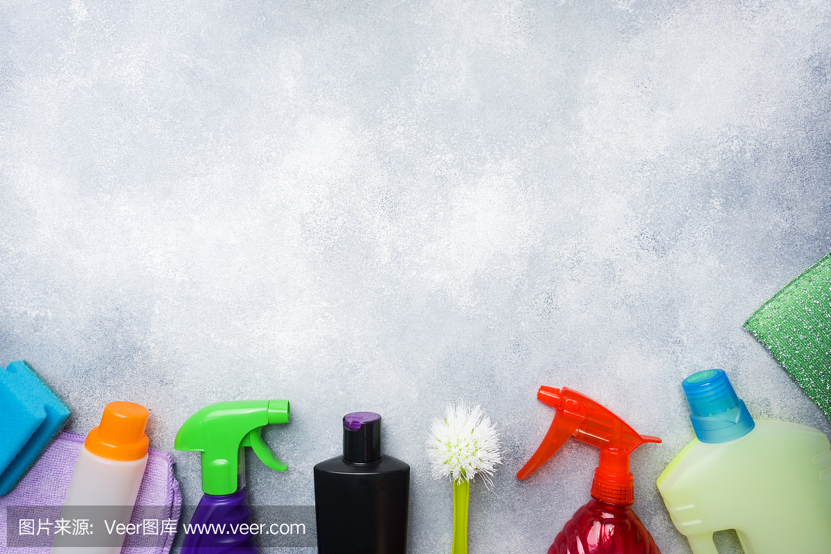 瓶子与洗涤剂,刷子和海绵在混凝土背景。色彩鲜艳的清洁产品。家庭清洁的概念。俯视图,复制空间。